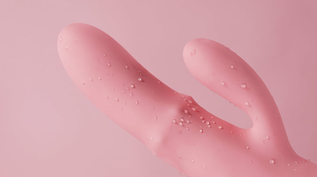 Pink silicone rabbit vibrator with water droplets on a soft pink background