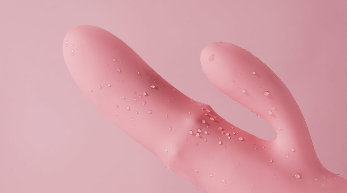 Pink silicone rabbit vibrator with water droplets on a soft pink background